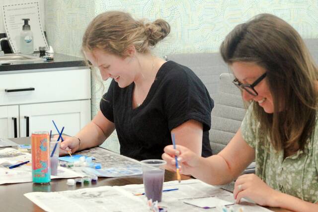Catherine Klein, left, and Layne Manson enjoy painting some individual mosaic pieces. Their work will be included in the putting together of a large mosaic of about 1,000 individual pieces, with the theme of Americana. It will be mounted on the north side on the VFW building and be visible from Sixth Street.